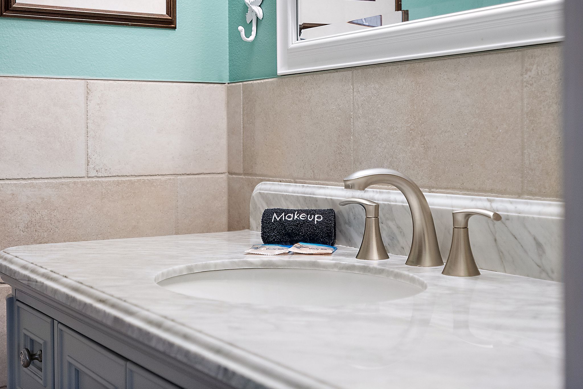 A bathroom with a marble sink, two faucets, and a towel rack labeled "Makeup".