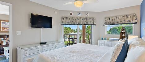 A bedroom with a bed, a TV, a dresser, and a window with a view of greenery.