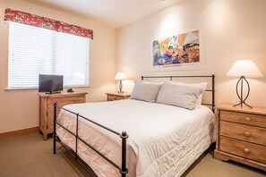 A bedroom with a bed, bedside tables, a television, and a painting on the wall. - Bridgepoint Condo 11 - Ketchum Condo Walk to River Run (Ketchum)