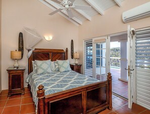Relax in a serene bedroom with a four-poster bed, ceiling fan, and wall-mounted air conditioning unit, offering a view of the lush landscape.