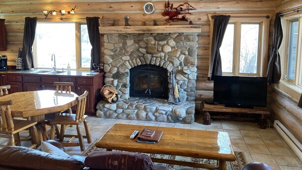 Un intérieur de chalet chaleureux avec une cheminée en pierre, des meubles en bois et un téléviseur.