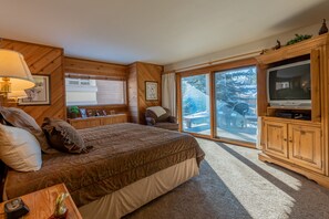 Cozy retreat with a large bed, wooden headboard, and television, offering a view of the snowy outdoors.