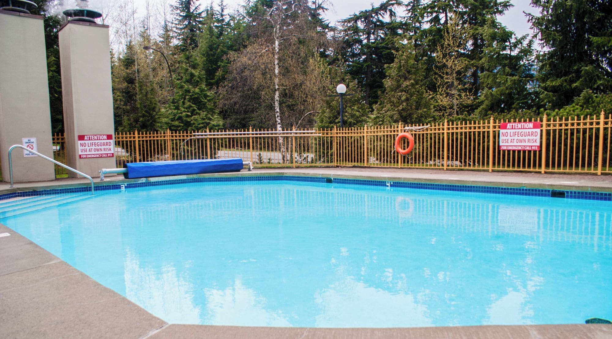 A swimming pool with a yellow safety fence, a lifeguard sign, and a 5 ft depth marker.