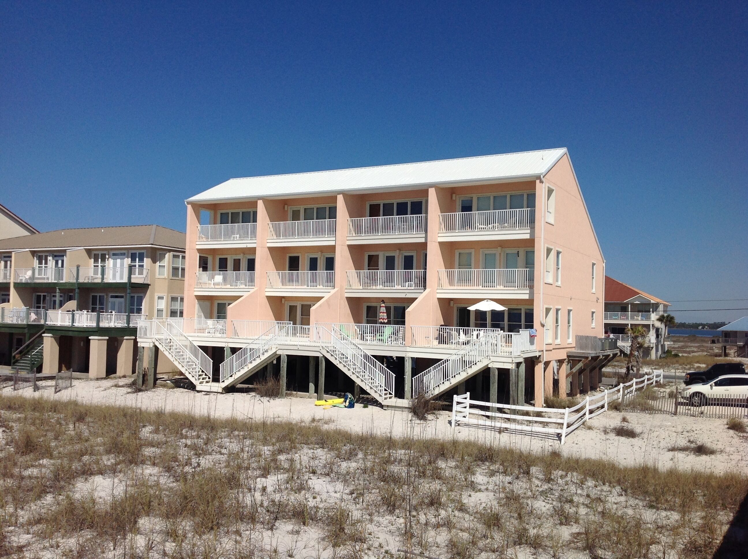 Un hôtel de plusieurs étages situé en bord de mer, doté de balcons, avec une plage de sable devant et un ciel bleu dégagé.