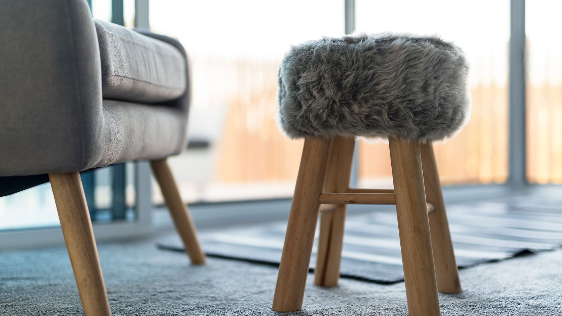 Ein modernes Wohnzimmer mit einem grauen Sofa und einem hölzernen Hocker mit Sitzfläche aus Fell.