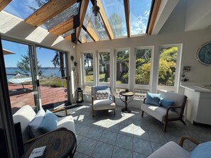 A sunlit room with a view of the sea, furnished with a sofa, chairs, and a small table. - Olympic Peninsula, from Coast to Forest, Scenic Hiking, Kayaking, Fishing, GEM. (Brinnon)