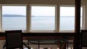 A room with three large windows offering a view of a calm body of water and a distant shoreline. - Olympic Peninsula, from Coast to Forest, Scenic Hiking, Kayaking, Fishing, GEM. (Brinnon)