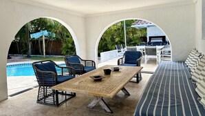 Un área de estar al aire libre cubierta, con piscina, sillones reclinables y una mesa.
