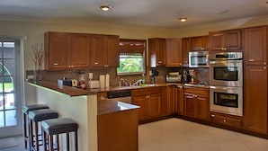 Una cocina moderna con armarios de madera, electrodomésticos de acero inoxidable y una zona con taburete de bar.