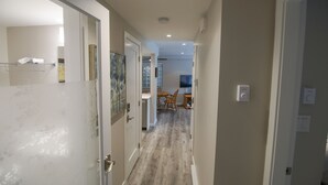 A hallway with a wooden floor, white walls, and a door on the left. There is a small table and chairs in the background. - Pool and Hot Tub Access, Newly Renovated Suite with Free Parking, WiFi (Whistler)