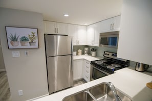 A modern kitchen with stainless steel appliances, white cabinetry, and a tiled backsplash. - Stoney Creek Northstar 8 (Whistler)
