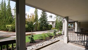 A covered outdoor area with a paved walkway, a railing, and a view of a residential street with trees and a house. - Pool and Hot Tub Access, Newly Renovated Suite with Free Parking, WiFi (Whistler)