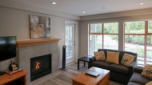 A living room with a fireplace, a sofa, a coffee table, and a TV. - Pool and Hot Tub Access, Newly Renovated Suite with Free Parking, WiFi (Whistler)