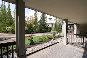 A covered porch with a view of a residential street, a lawn, and a house with a distinctive tower. - Stoney Creek Northstar 8 (Whistler)