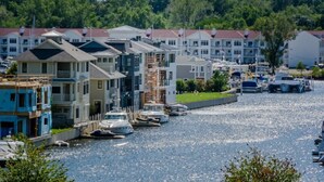 En småbåtshamn med båtar förtöjda längs en strandpromenad, omgiven av flerfamiljshus.