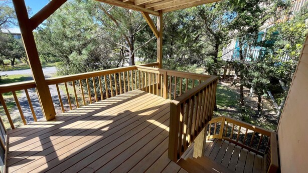 Um deck de madeira com guarda-corpo, cercado por árvores e um céu claro.
