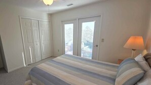 Quarto com uma cama grande, mesa de cabeceira, abajur, armário e porta de vidro deslizante para o exterior.