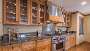 A kitchen with wooden cabinets, a granite countertop, stainless steel appliances, and a window with blinds. - Captivating Historic Cottage with Fireplace (Sun Valley)