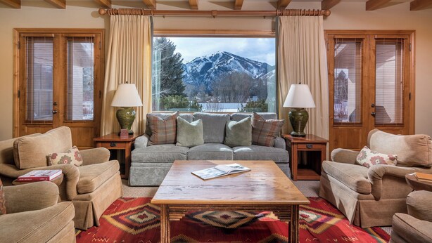 A cozy living room with a sofa set, a coffee table, and lamps. A window offers a view of snow-capped mountains. - Captivating Historic Cottage with Fireplace (Sun Valley)