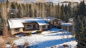 A house with a snow-covered roof, surrounded by trees and a mountainous backdrop. - Captivating Historic Cottage with Fireplace (Sun Valley)