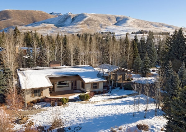 A house with a snow-covered roof, surrounded by trees and a mountainous backdrop.