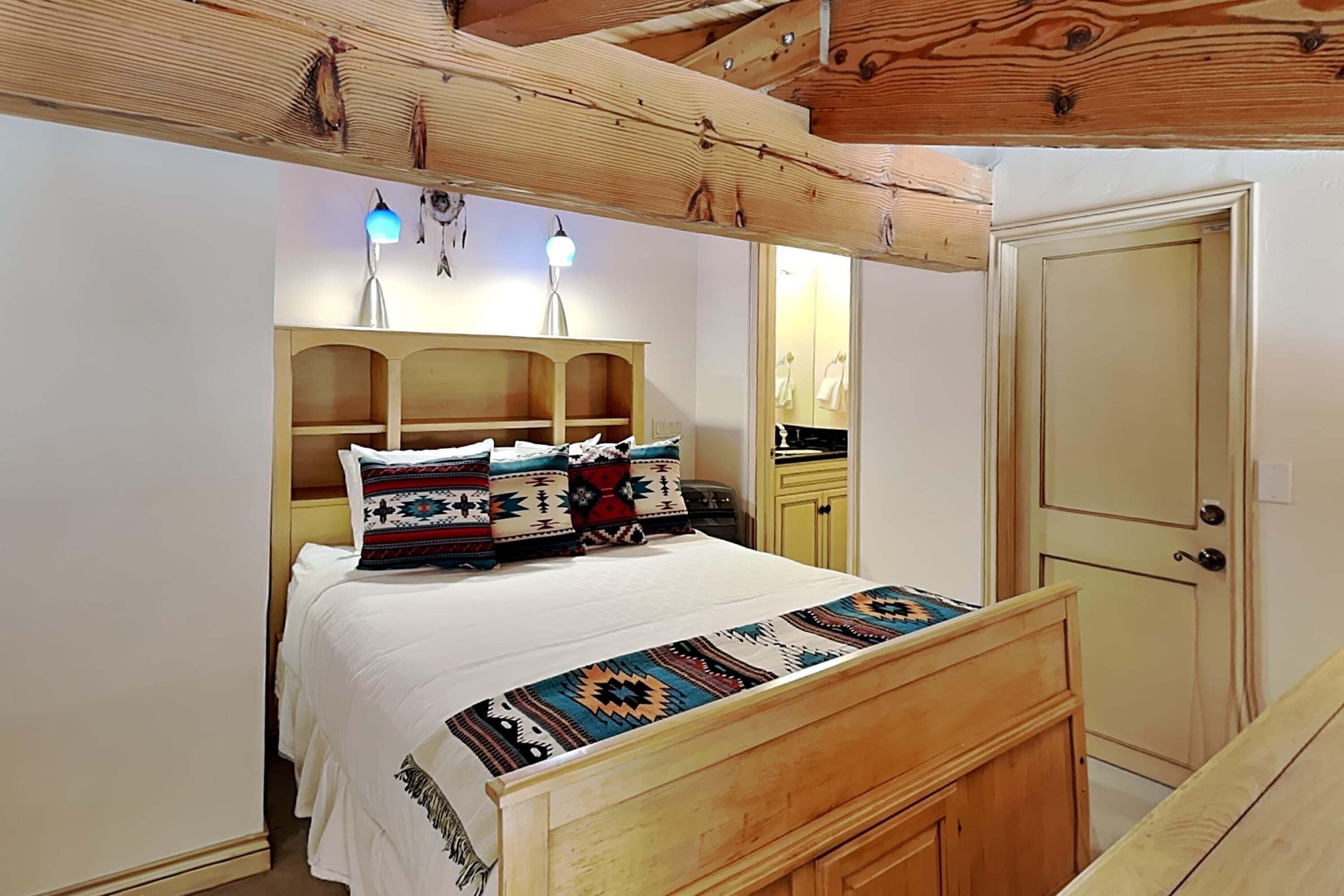Un dormitorio con cabecera de madera, una cama con ropa de cama estampada, una mesita de noche y un armario.