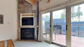 A living room with a stone fireplace, a flat-screen TV, and a sliding glass door leading to an outdoor deck.