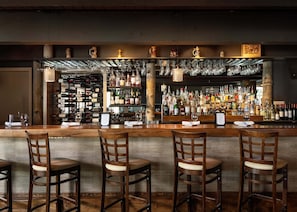 A bar with wooden chairs, a counter with bottles, and hanging glasses.