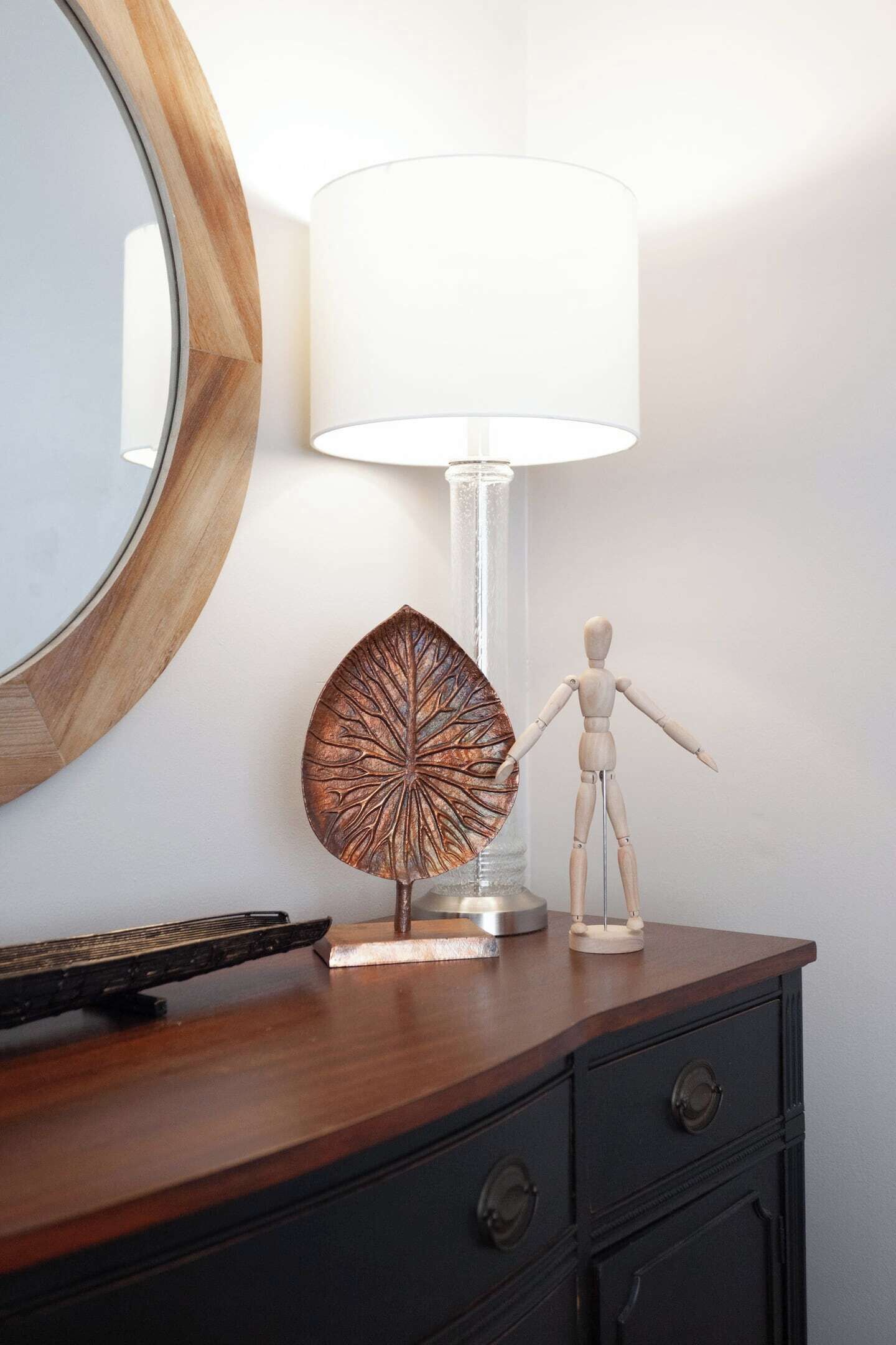 Un aparador de madera con un espejo, una lámpara y una figura de madera.