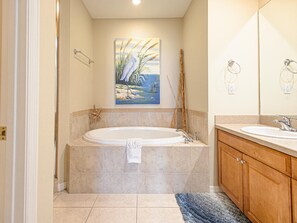 A bathroom with a large bathtub, wooden cabinets, and a painting of a bird and reeds on the wall.
