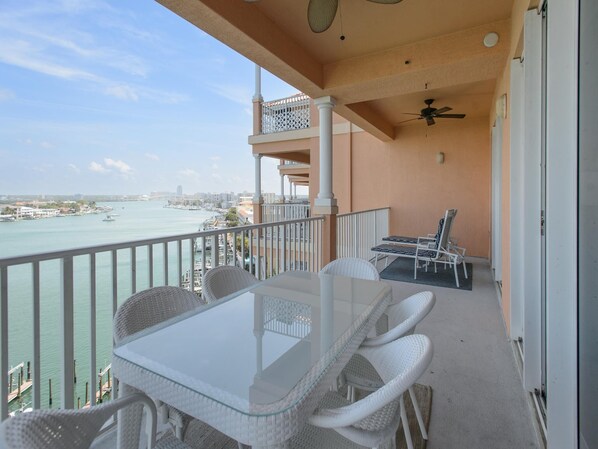 A balcony with a glass table and chairs, overlooking a marina and cityscape.