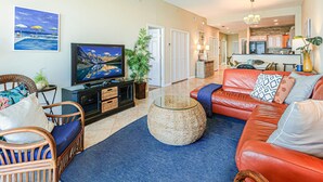 A living room with a television, a red sofa, wicker chairs, and a blue rug.
