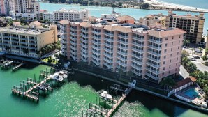A high-rise hotel with multiple balconies, a marina with boats, and a beach in the background.