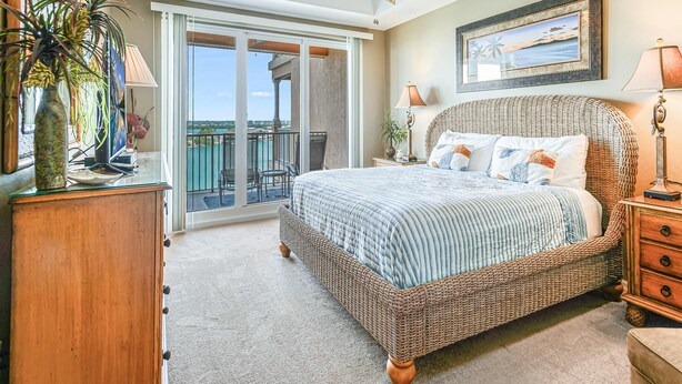 A bedroom with a large bed, a balcony with a view, and a ceiling fan.