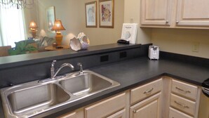 A kitchen with a double sink, wooden cabinets, and a countertop. - The Inn at Dauphin Island 102 Walk right out to Pools and Beach! (Dauphin Island)