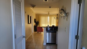 A hallway leading to a kitchen with a dishwasher, a ceiling fan, and a dining area with a table and chairs. - The Inn at Dauphin Island 102 Walk right out to Pools and Beach! (Dauphin Island)