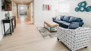 A modern living room with a sofa, a coffee table, and a patterned ottoman. There is a hallway leading to another room. -  LOCATION! COMPLETE REHAB Great pool, close to north bean pt., twin family rooms (Anna Maria)