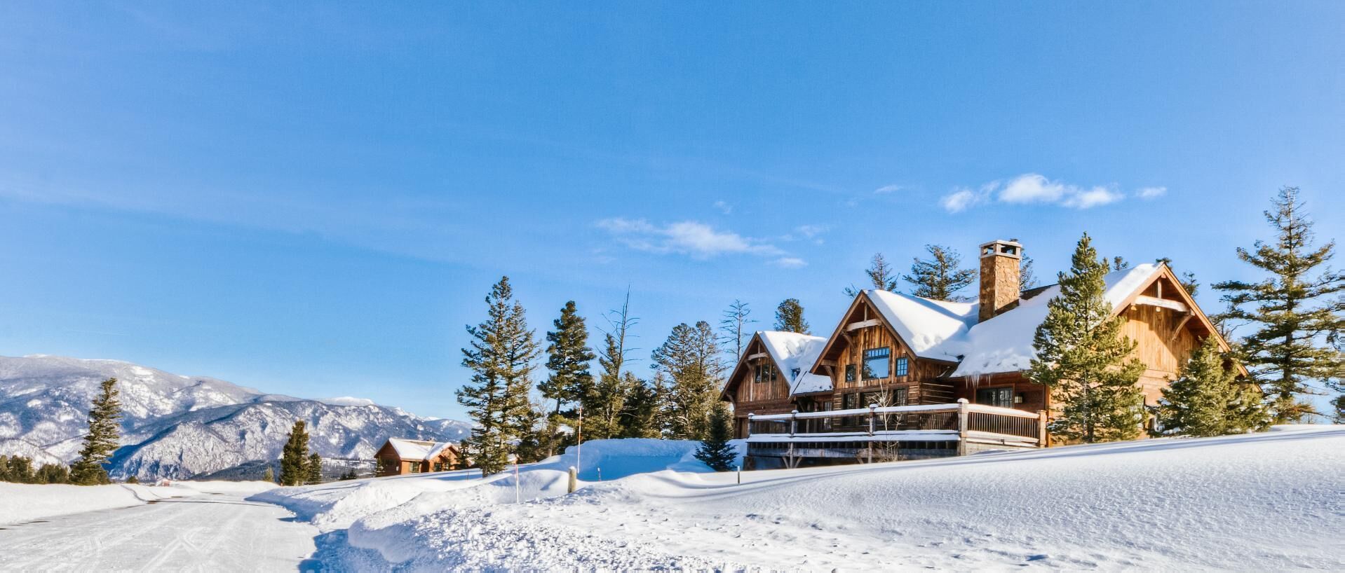 Un grand chalet en bois, doté de nombreuses cheminées, entouré d’arbres et de montagnes couverts de neige.