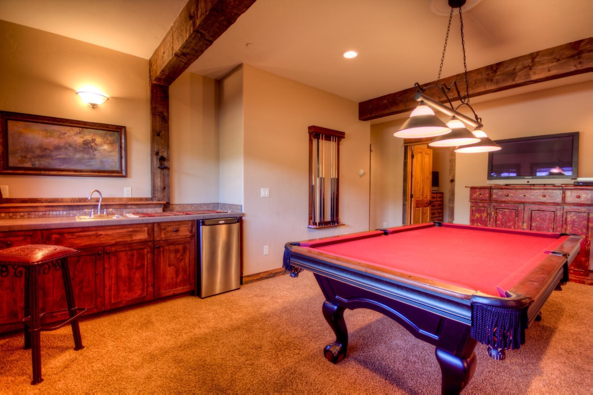 Une table de billard dans une pièce dotée de meubles en bois, d’un évier et d’un téléviseur.