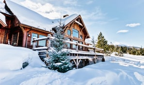 A wooden lodge with a snow-covered roof and a balcony. - Home with Mountain Views, Hot Tub, Garage and Pool Table! (Big Sky)