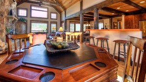 A rustic dining area with a large wooden table, bar stools, and a stone fireplace. - Mountain View | Hot Tub | Game Room (Big Sky)