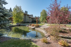 Escape to a serene outdoor oasis with a tranquil pond and walking path, surrounded by lush trees and autumnal foliage.