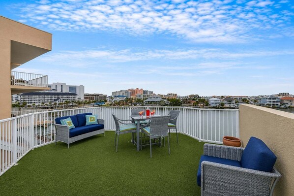 Un balcon extérieur avec une balustrade blanche, un canapé bleu, une table avec des chaises et une vue sur le paysage urbain.