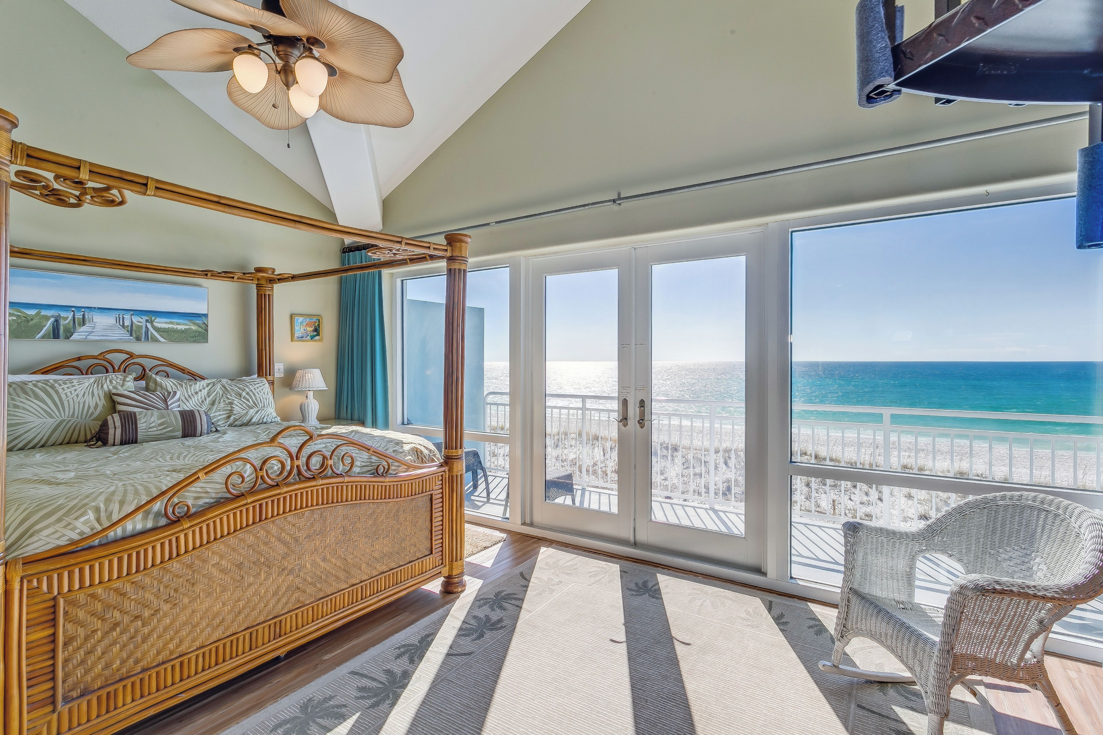 Une chambre spacieuse avec un grand lit, un balcon donnant sur la plage et un fauteuil en osier.