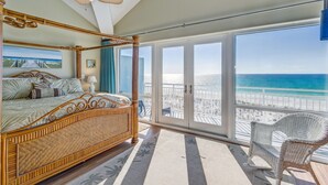 Un dormitorio amplio con una cama grande, un balcón con vistas a la playa y una silla de mimbre.
