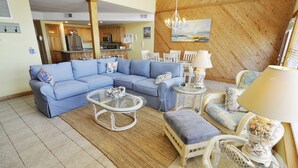 A living room with a sectional sofa, a coffee table, and a dining area with chairs and a table. - Almost Heaven: Colorful sunsets and views of Portsmouth Island. (Ocracoke)