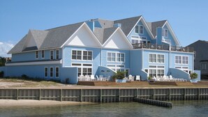 A large, two-story house with a balcony, situated by a body of water. - Almost Heaven: Colorful sunsets and views of Portsmouth Island. (Ocracoke)
