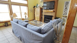 A living room with a sectional sofa, a fireplace, a television mounted on a wooden wall, and a 'BEACH' sign. - Almost Heaven: Colorful sunsets and views of Portsmouth Island. (Ocracoke)
