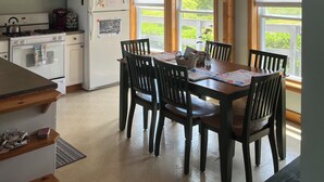 Une cuisine avec des poutres en bois, des meubles blancs, une cuisinière et un coin repas comprenant des chaises et une table.