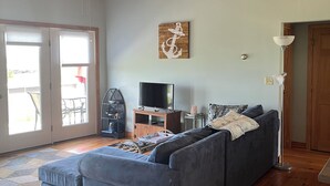 Un vaste salon doté d’un grand canapé d’angle gris, d’un plancher en bois, d’un ventilateur de plafond et d’un téléviseur posé sur un meuble en bois.